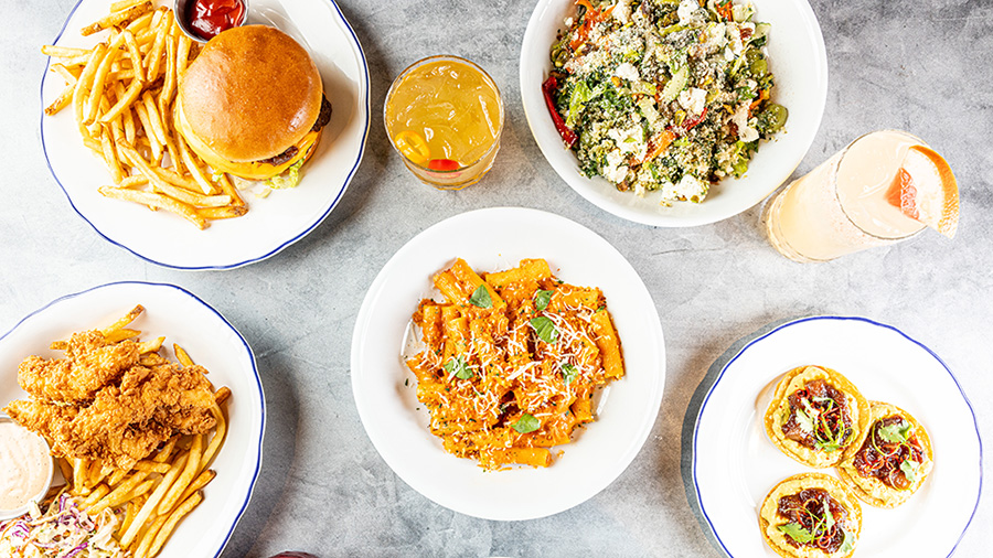 Plates of burgers, pasta, salads and fried chicken are arranged on a marble table