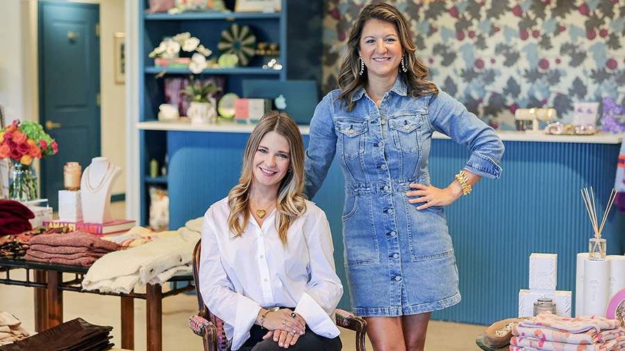 Two women stand in the store they own, filled with jewelry, home decor and clothing.