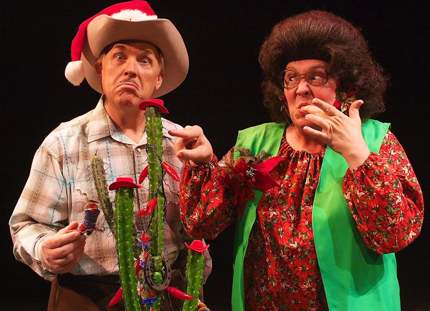 A man in a cowboy hat with a Santa hat and a woman stand behind a cactus sporting tiny red cowboy hats