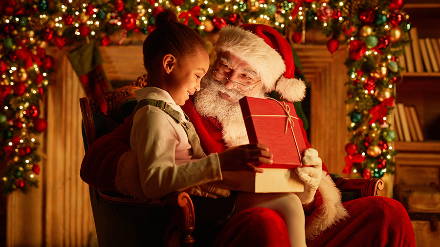 A girl meeting Santa in front of a fireplace covered in Christmas garland