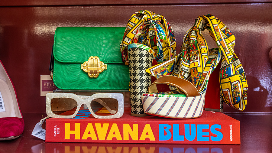 A designer clutch, patterned high heels, sunglasses and book are arranged on a boutique shelf