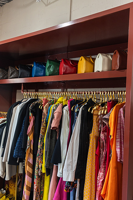 A rack of clothing hangs beneath a shelf with designer handbags