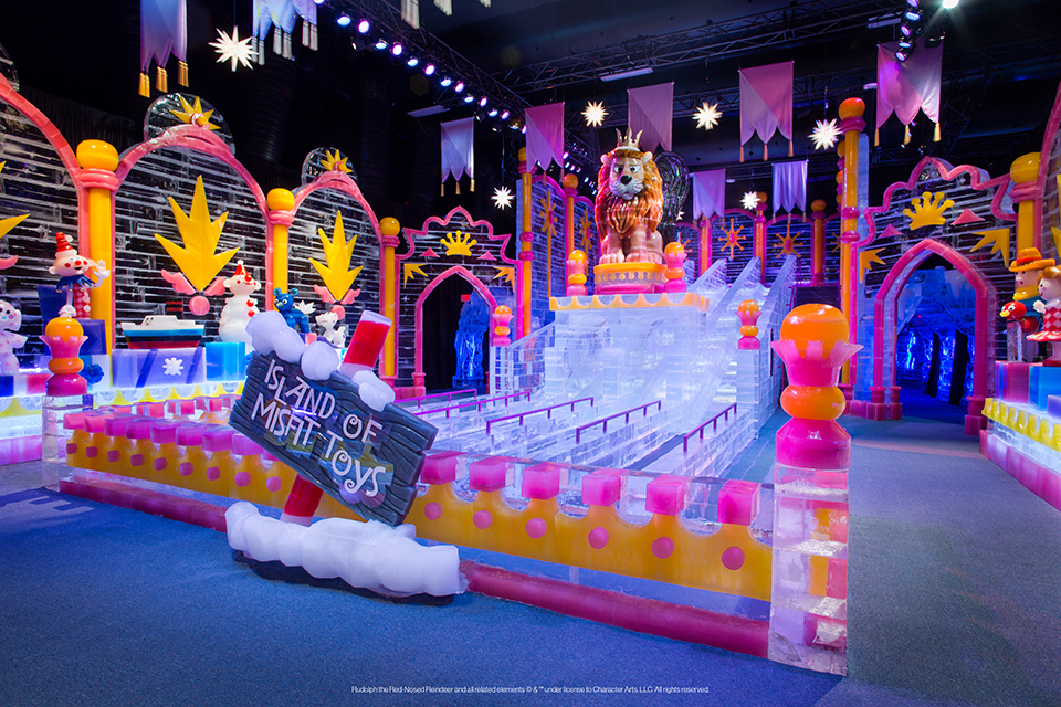 The Island of Misfit Toys, made out of ice. There is a sign in the foreground and a large lion in the background.