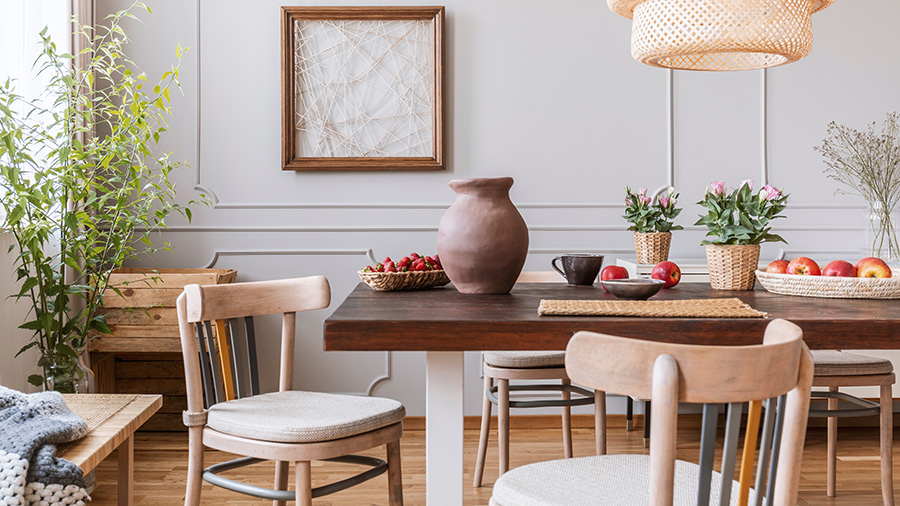 A dining room with apples and a vase on the table, unique chairs and textured art on the wall