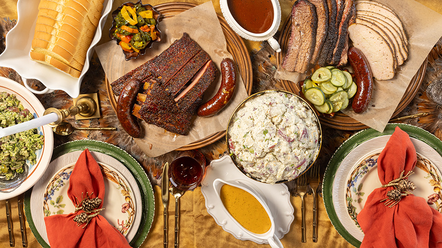 A Thanksgiving table spread with sausage, brisket, potato salad, pickles, gravy, bread and sides