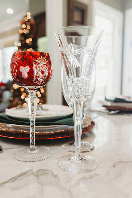 Red and clear crystal glasses stand in front of holiday place settings