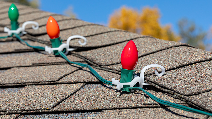 Large red, orange and green Christmas lights are hung on a roof with clips