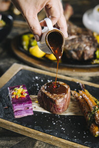 Pouring demi-glace onto a steak with vegetables