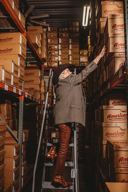 Susan Maddox stands on a ladder at The Best Hat Store.