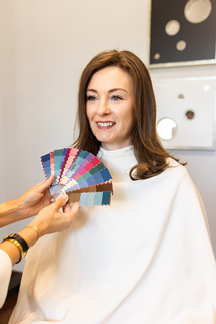 A custom color fan is held up to a client's face to show her ideal colors.