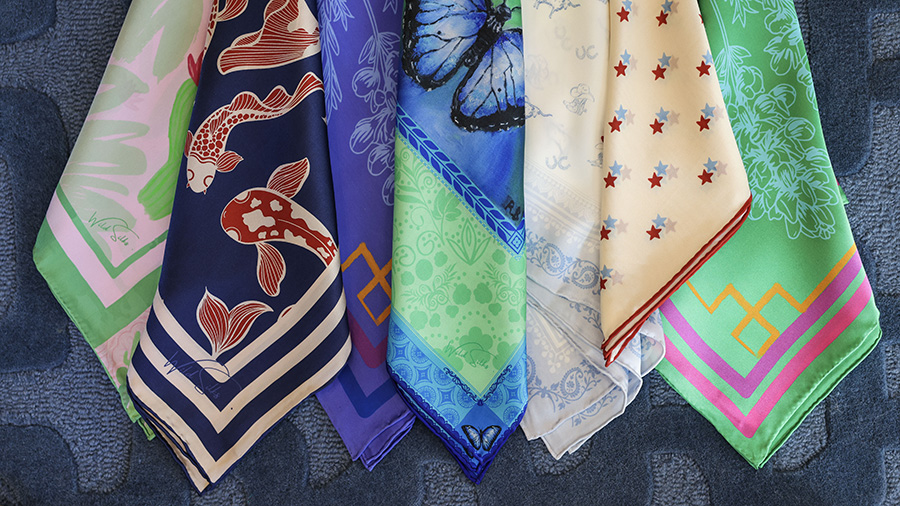 Seven of Christi Braswell's silk scarves, featuring koi, butterfly, Longhorn, star and floral patterns.