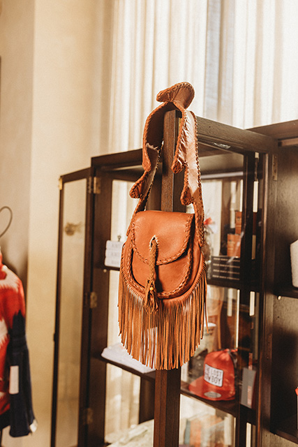 A beautiful brown leather bag features braided trim and fringe.