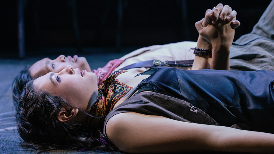 Two actors lie on the ground holding hands in "Hadestown"