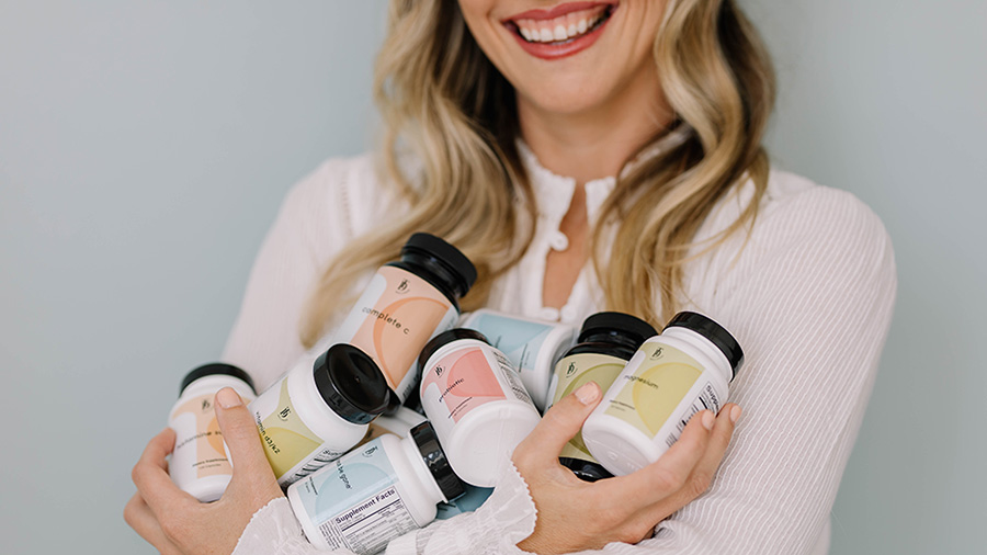 Taylor Dukes holds bottles from her line of wellness supplements