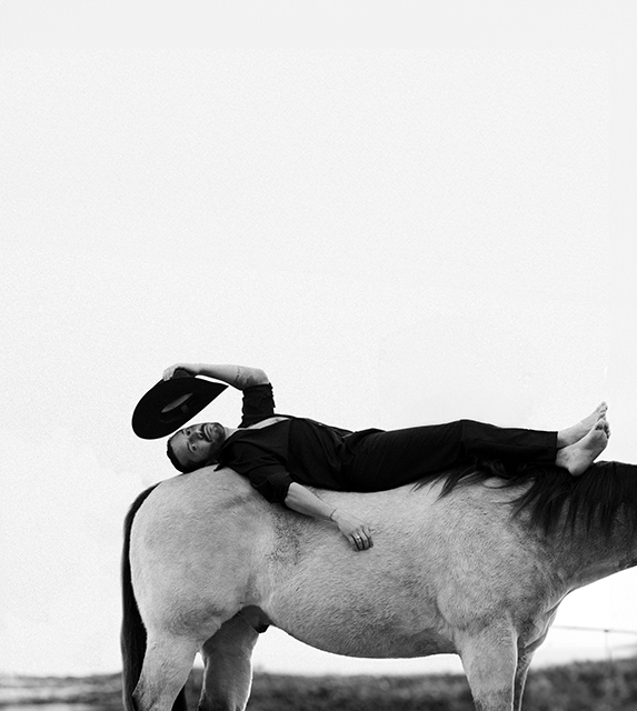 Emerson Miller lies on top of a horse, tipping his hat